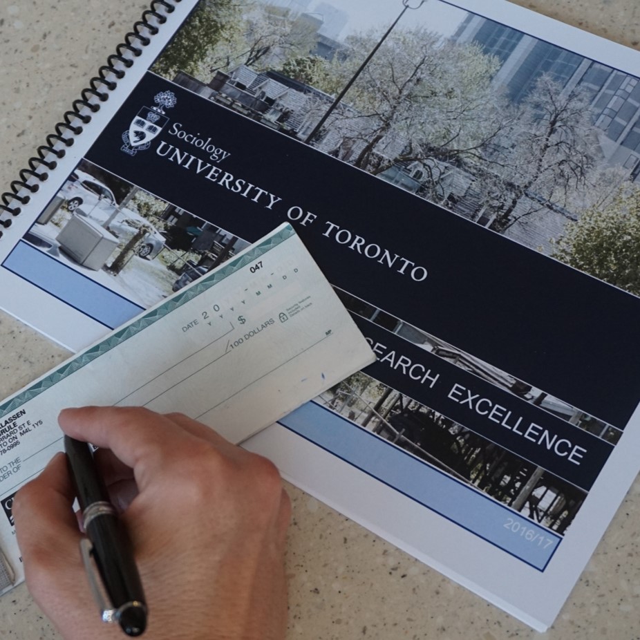 A booklet entitled "Research Excellence" rests beneath a cheque. A hand is visible with a pen, as though about to sign it.