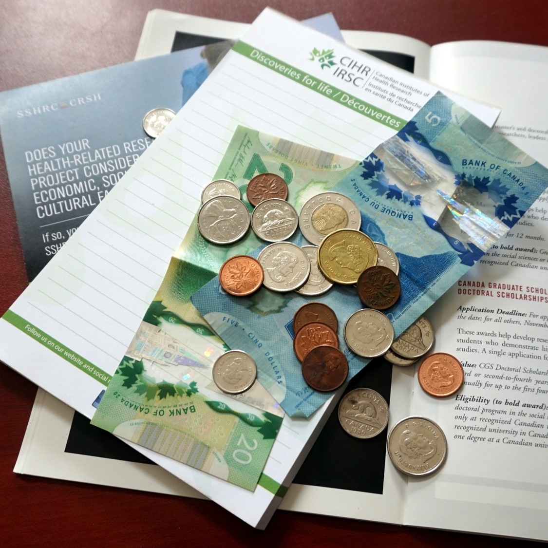 Canadian bills and coins lie scattered on a table with brochures
